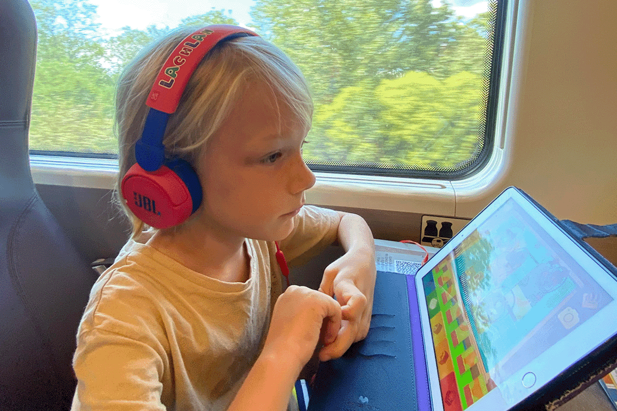 little boy using a learning app on an ipad while riding in a train