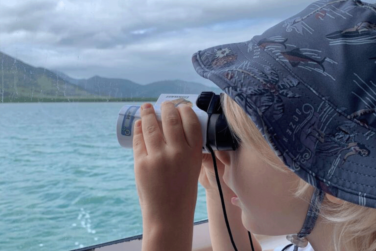 small boy holding binoculars looking out to sea